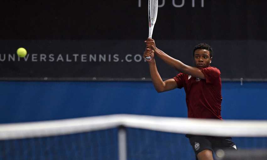 A young man swings a tennis racket at the ball with both hands