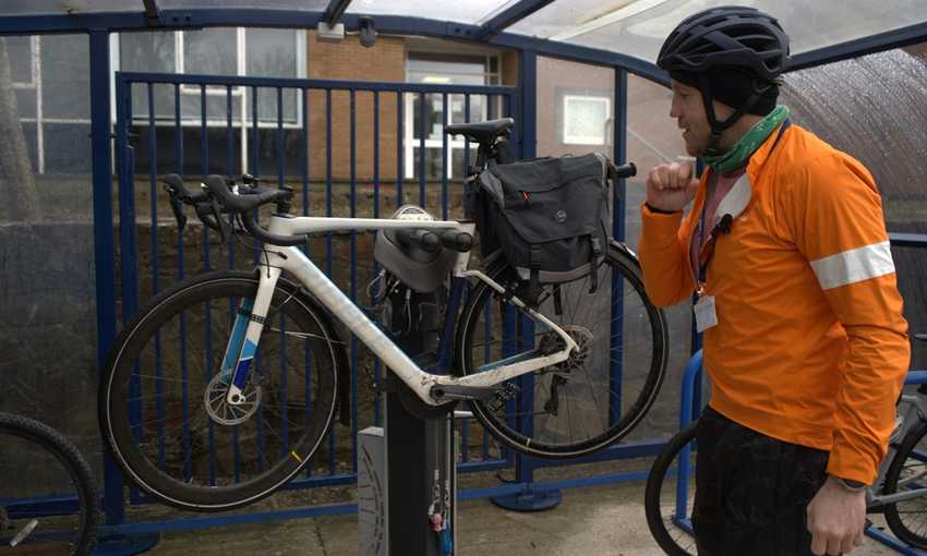 A man in high visibility clothing inspects his bicycle on a lifted stand