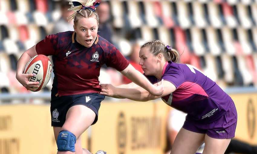 A Cardiff Met player runs with a rugby ball while holding off an opponent with their arm during a rugby match