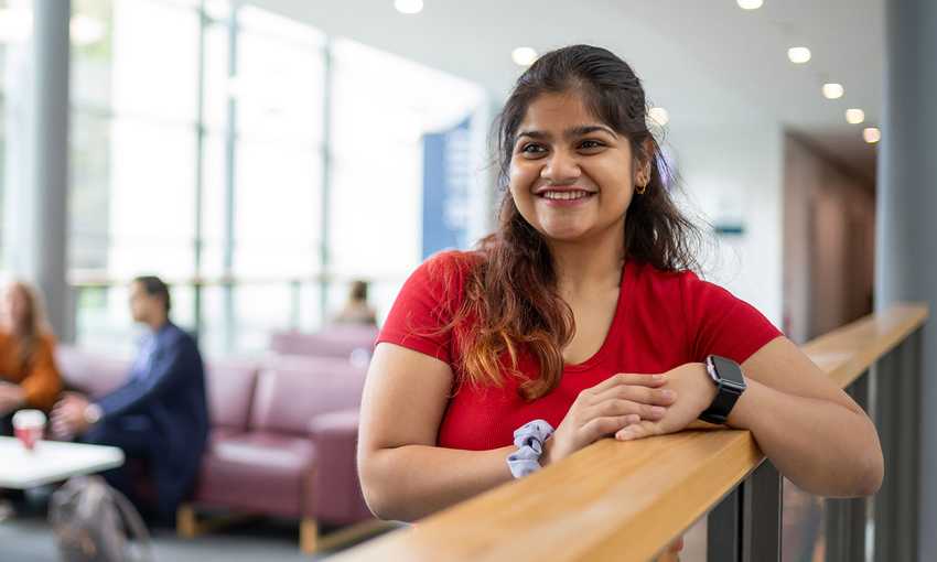 A cheerful young woman in a red shirt poses in a bright hallway, exuding positivity and warmth.