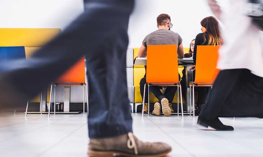 A group of people engaged in conversation while seated at a table in a communal area setting.