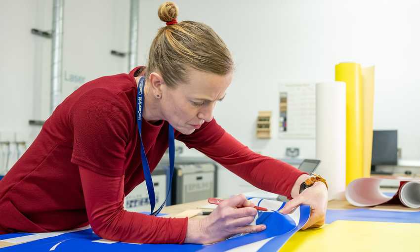 A woman focused on creating artwork on a large sheet of paper, showcasing her creativity and dedication.