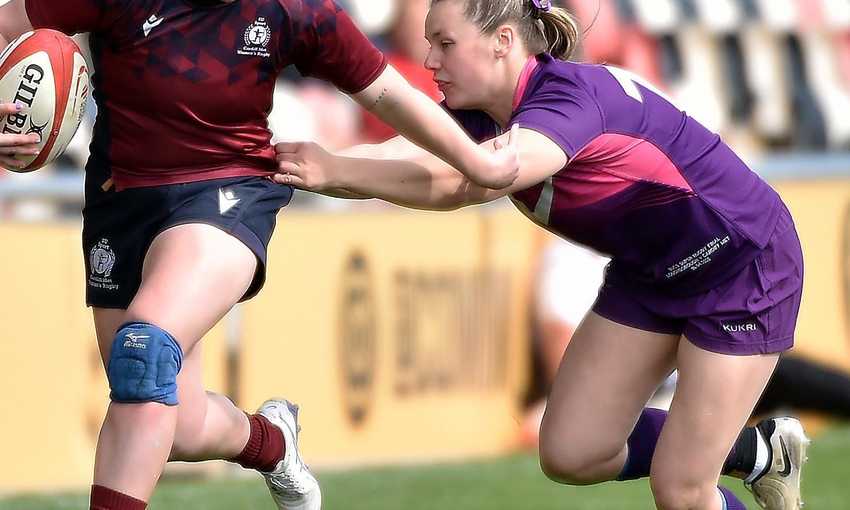 A Cardiff Met player runs with a rugby ball while holding off an opponent with their arm during a rugby match
