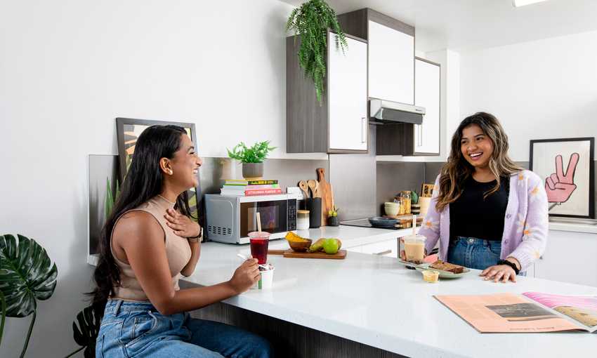 Two young adults sitting and talking at a kitchen island while preparing food