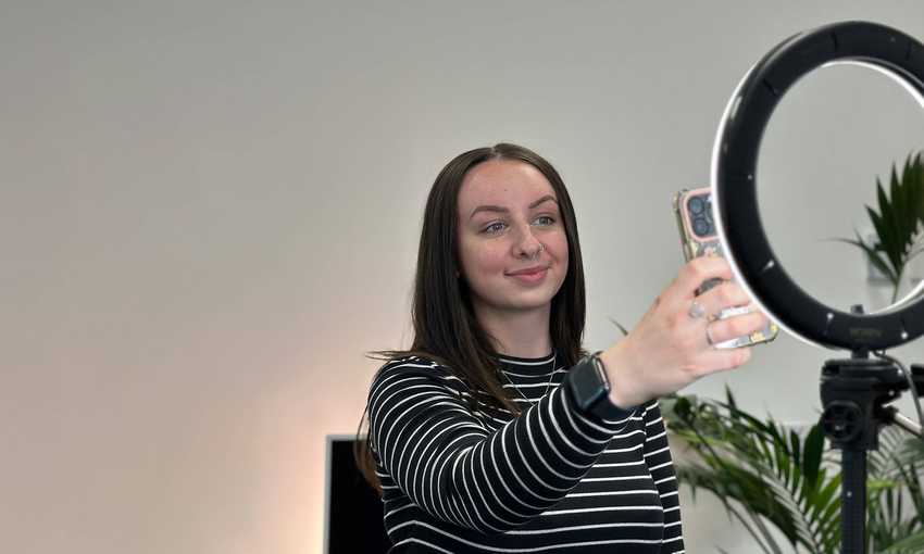 A person filming themselves using a mobile, illuminated by a ring light.