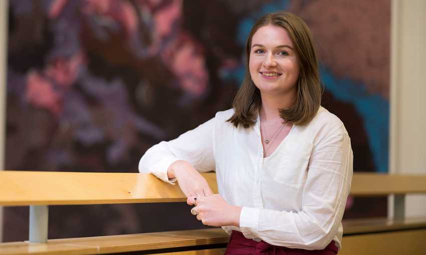 A young woman in a white blouse leans with one arm on a wooden railing.