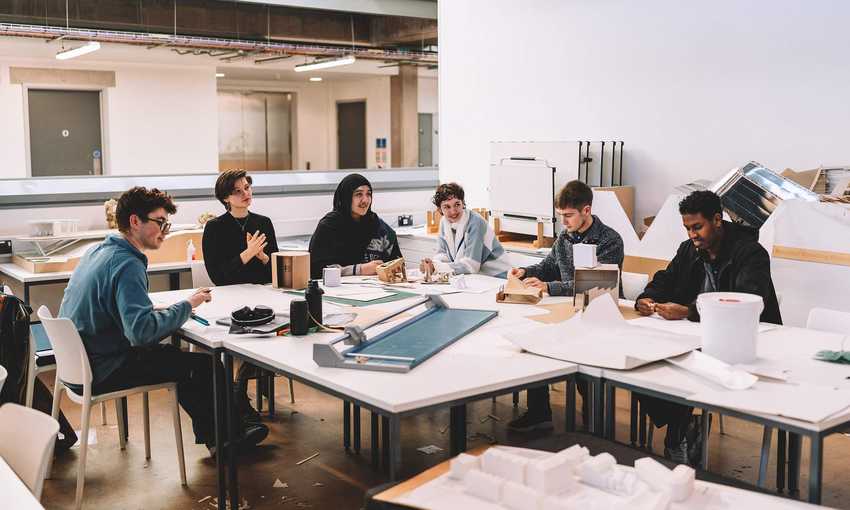 Group seated around studio tables examining models and papers in a large workspace.