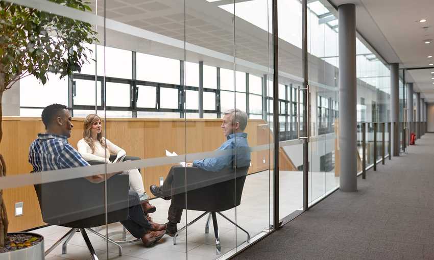 Three people sit facing one another in chairs during a meeting.