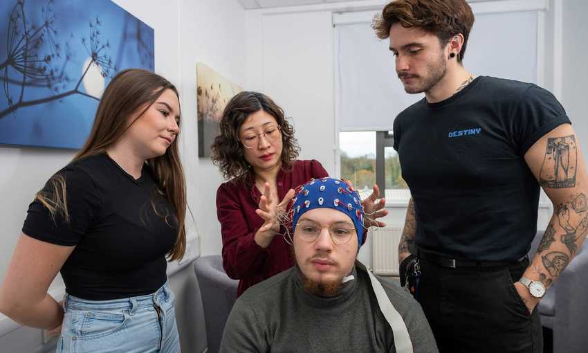 A seated person wearing an EEG cap, as three other people look on.