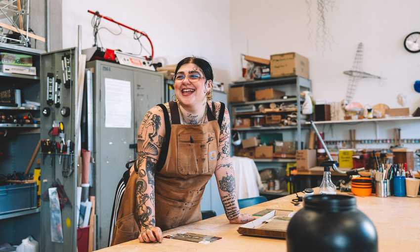 A student leans on a workbench. Behind them are metal cabinets, shelves and a variety of tools, including screwdrivers and spirit levels.