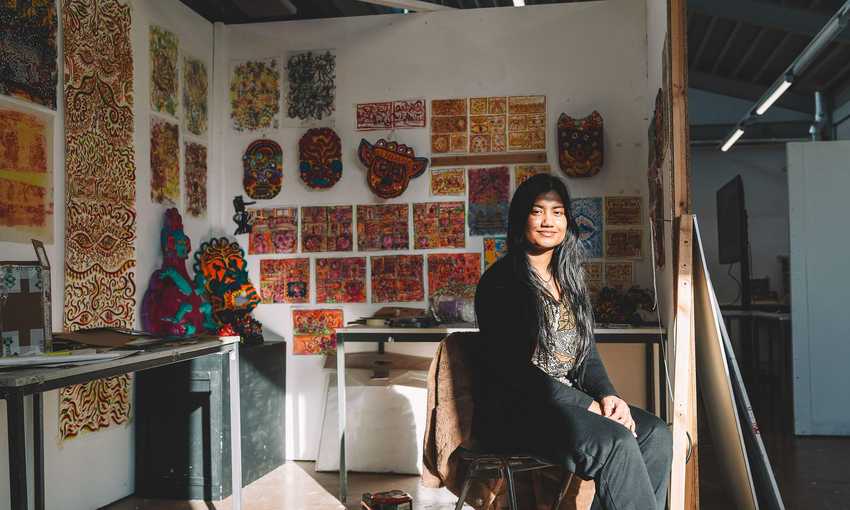 A student sits in front of a wall filled with various pieces of colourful artworks.