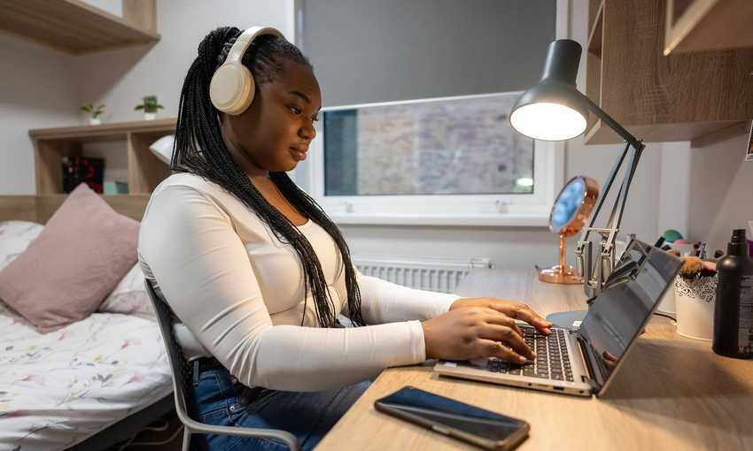A woman wearing headphones sits at a desk, focused on her laptop while working or studying.