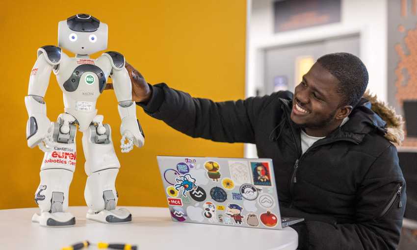 Student with laptop next to robot