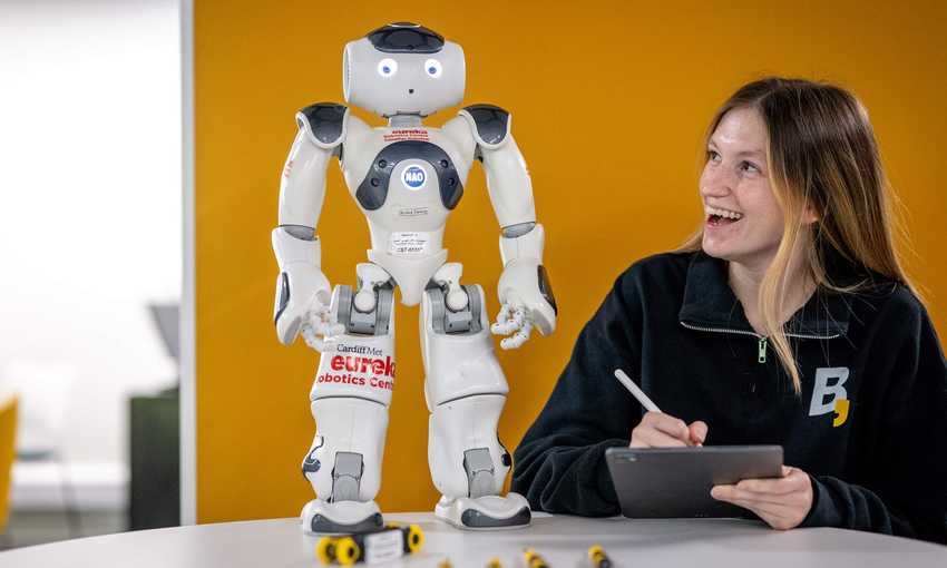 Person holding a tablet and stylus while looking up at a small humanoid robot.
