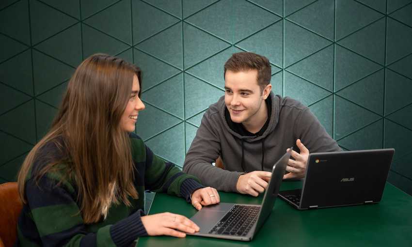 Two students with laptops in conversation