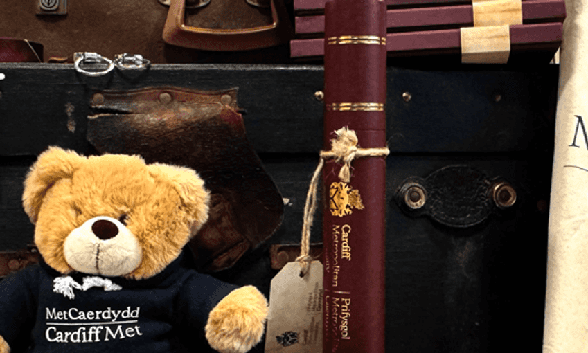 A display of Cardiff Metropolitan University merchandise, including branded plush bears, tote bags, and ties