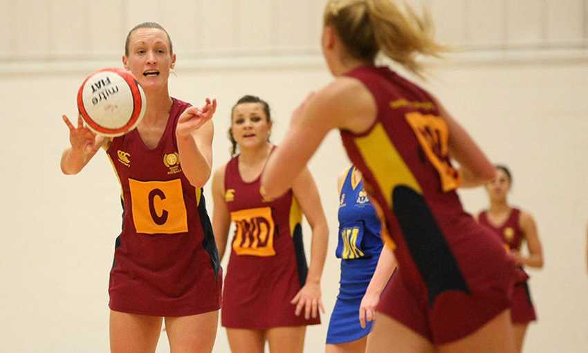 A group of women engaged in a netball game inside a gymnasium, showcasing teamwork and athleticism.