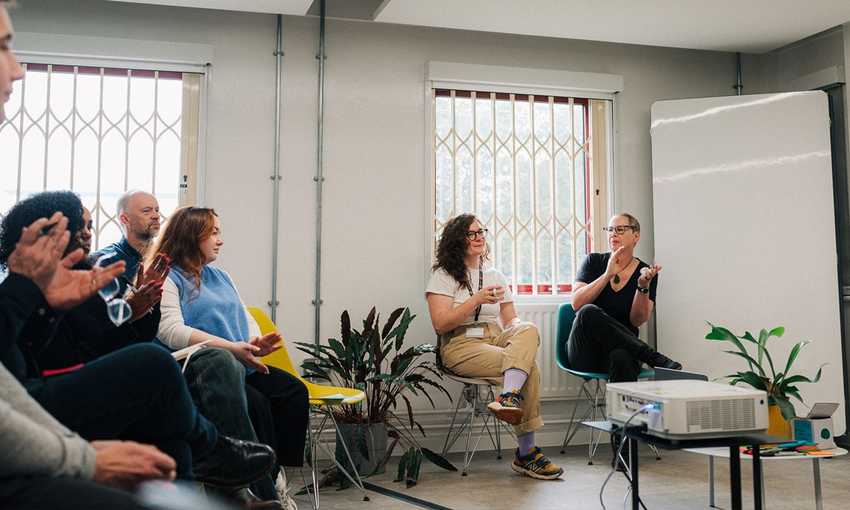 A woman holding a microphone speaks to a room of seated attendees
