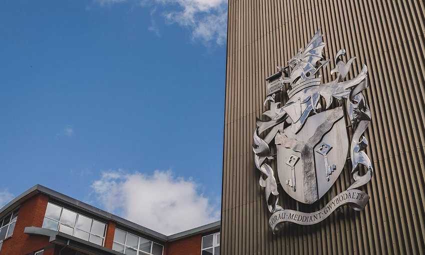 Cardiff Metropolitan University crest in silver on the side of a wood panelled building