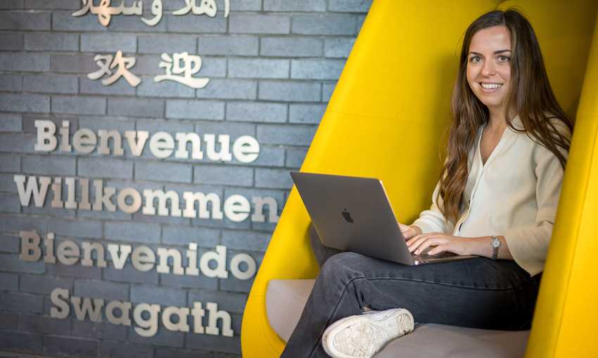 A woman working on her laptop while comfortably seated in a bright yellow chair, showcasing a lively atmosphere.