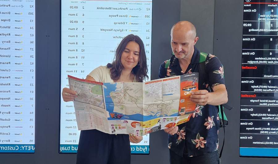Two individuals inspect a buss map in a busy bus station