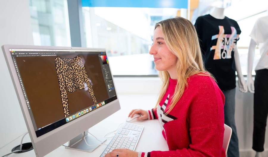 A person sat at a desk in front of a Mac computer.
