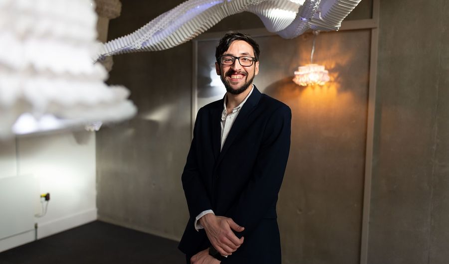 A young adult in a black suite stands underneath an art installation