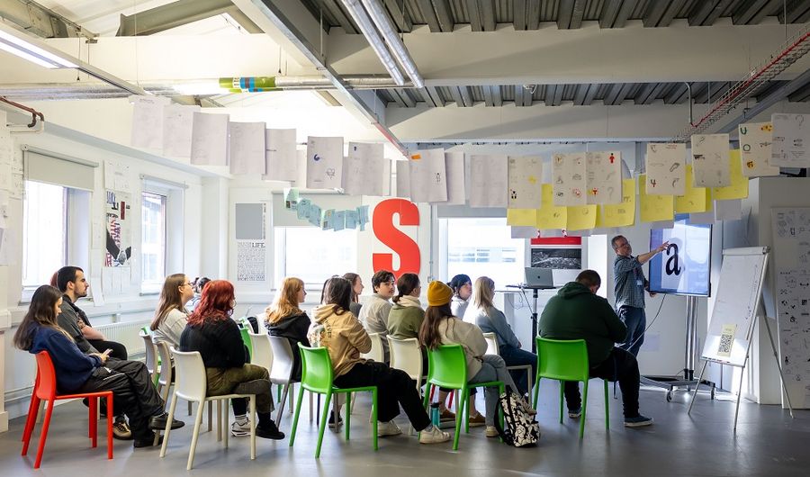 A group of young adults seated for a lecture in an open spaced workshop