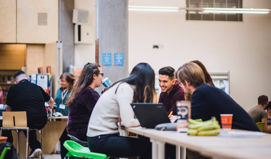 A group of five students sit around a table talking and smiling