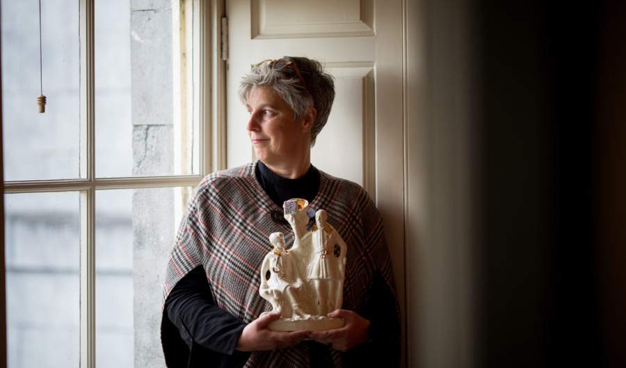 A woman looks out of a window to her right while holding a large white statue with both hands