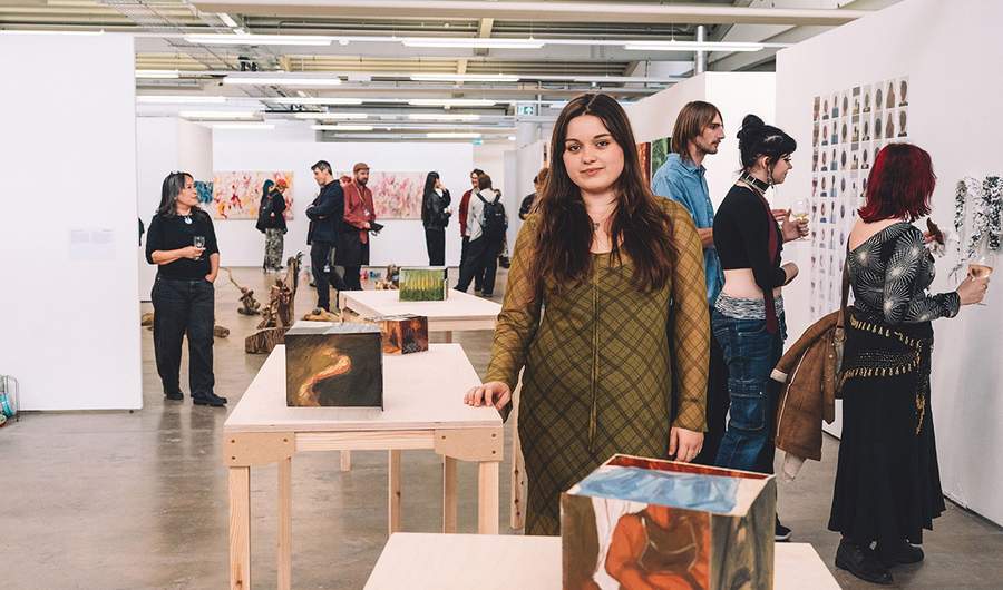 A woman stands in front of an art display, observing the various pieces with interest and contemplation.