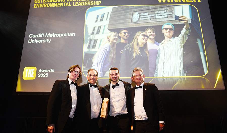 Cardiff Met staff accept an environmental leadership award on stage beneath a winner announcement screen.