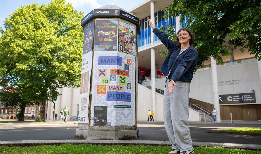A Cardiff Met student poses next to a poster display stand in the city