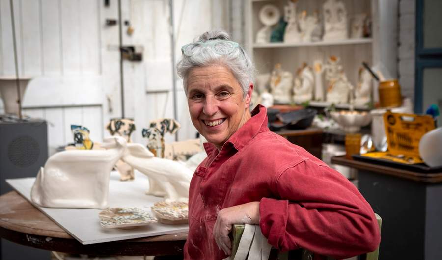 A woman working at a table of ceramics turning around to face the camera
