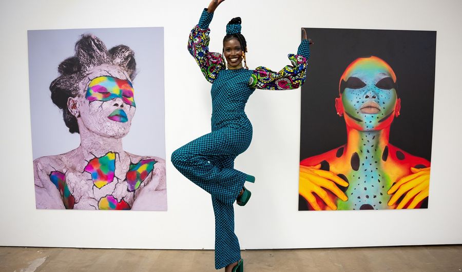 A young woman in a check blue dress with floral stands in between two displayed artworks