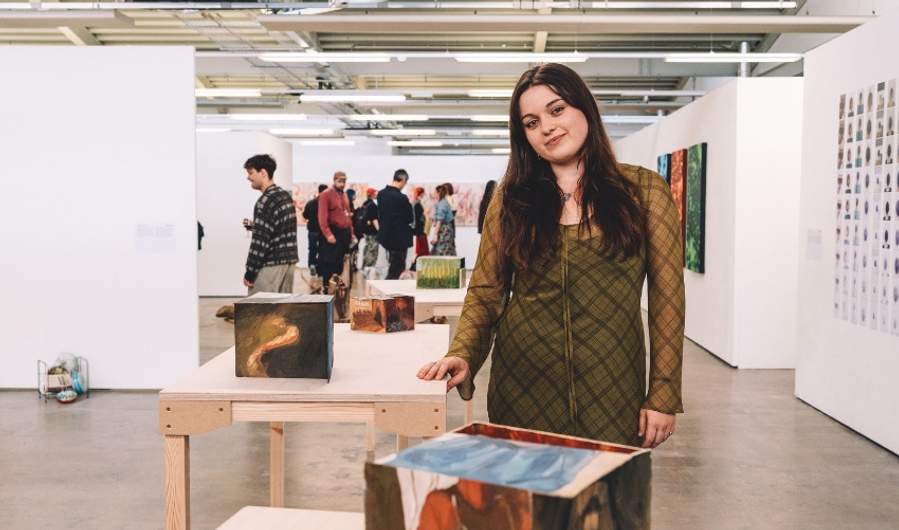 A woman stands in front of an art display, observing the various pieces with interest and contemplation.