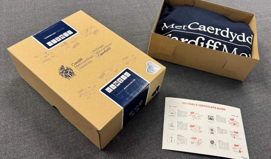 Two cardboards boxes, one opened and containing a Cardiff Met navy hoodie, on a carpeted floor