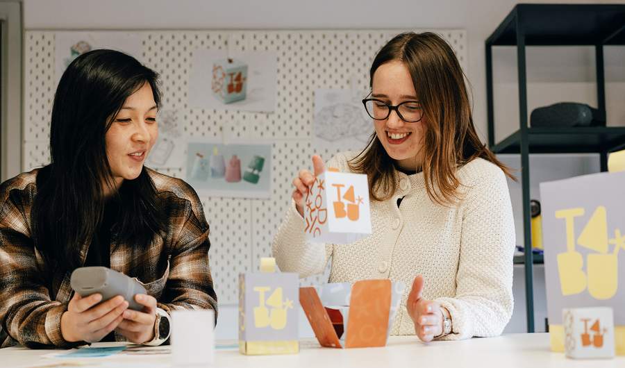 Two women engaged in conversation while seated at a table, with paper boxes placed between them.