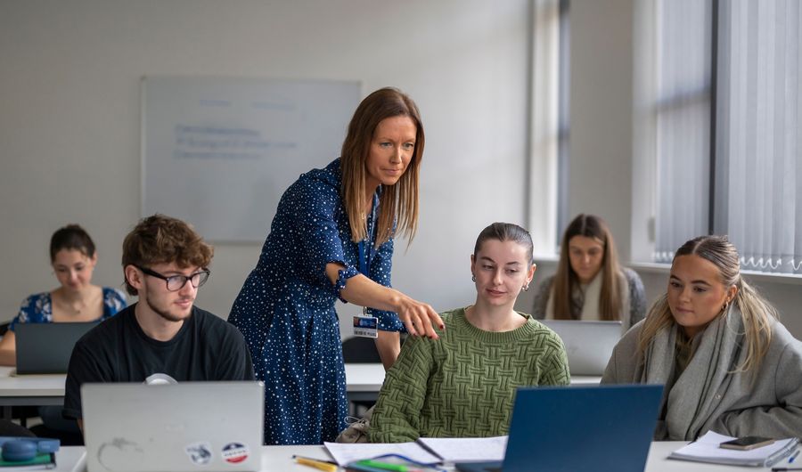 A lecturer points to the laptop of a student sat at a row of desks during a seminar