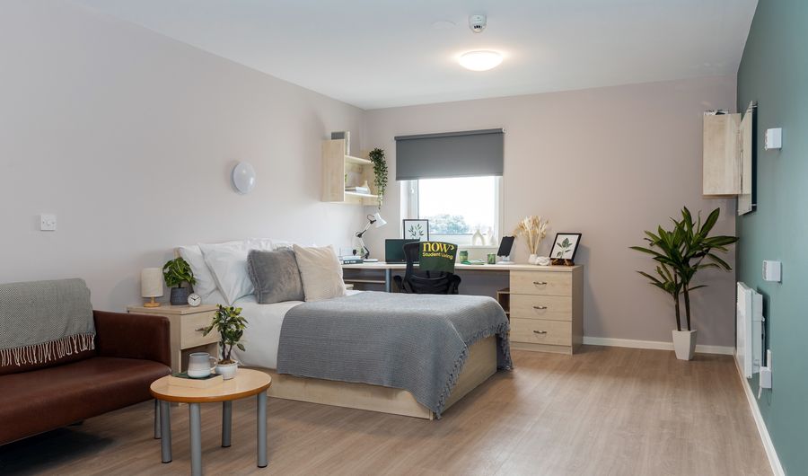 A large open bedroom complete with bed, study desk and sofa