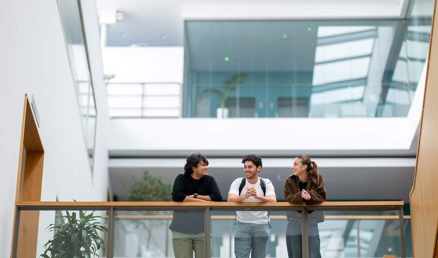 Three students talking while leaning over a mezzanine railing in the Cardiff School of Management