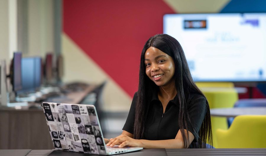 A young woman sits at a desk and works on their laptop
