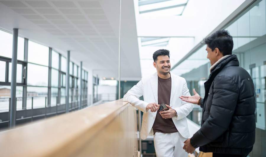 Two people engaged in conversation in a brightly-lit atrium space.