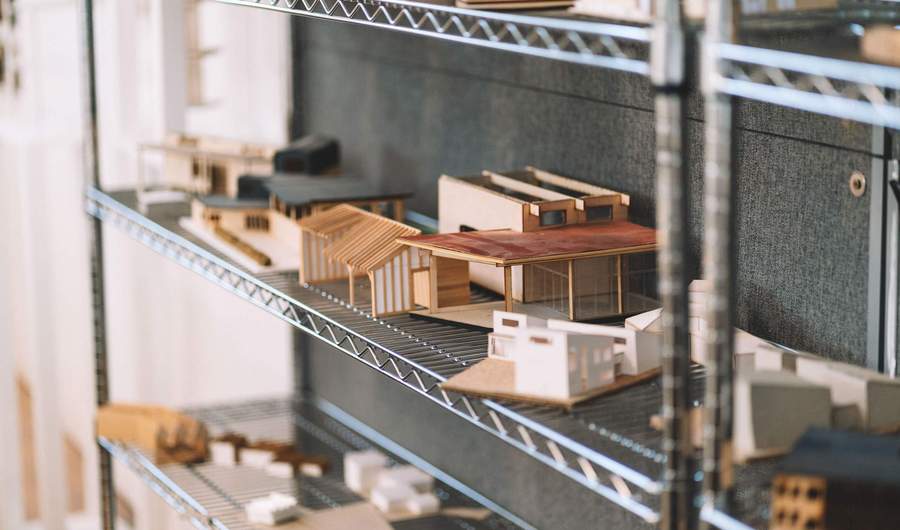A collection of small architectural models of buildings, arranged on wire shelves.