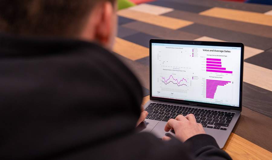 A close-up of a laptop computer. On the laptop screen are line and bar charts showing sales data.