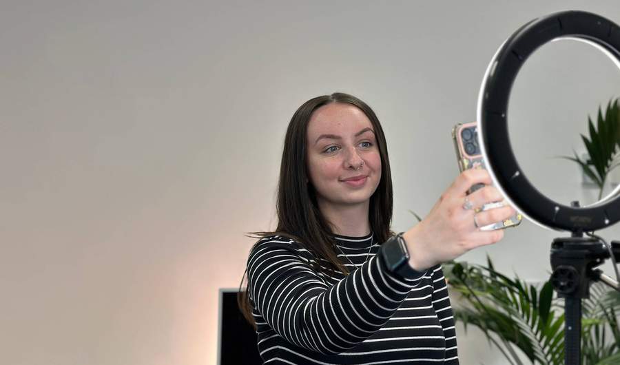 A person filming themselves using a mobile, illuminated by a ring light.