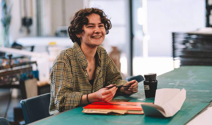 A young person sits at a table. In front of them are cutting mats and a notepad.