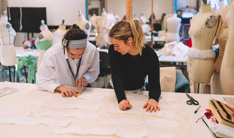 Two students working with fabric patterns. There are several mannequins in the background.