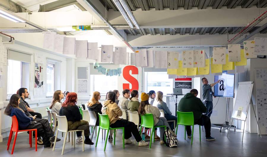 A group of young adults seated for a lecture in an open spaced workshop.