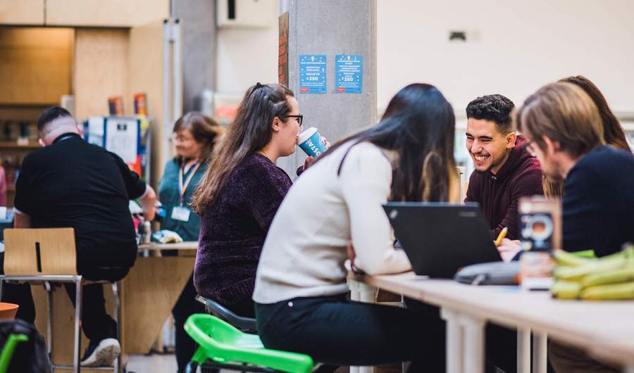 A group of five students sit around a table talking and smiling.
